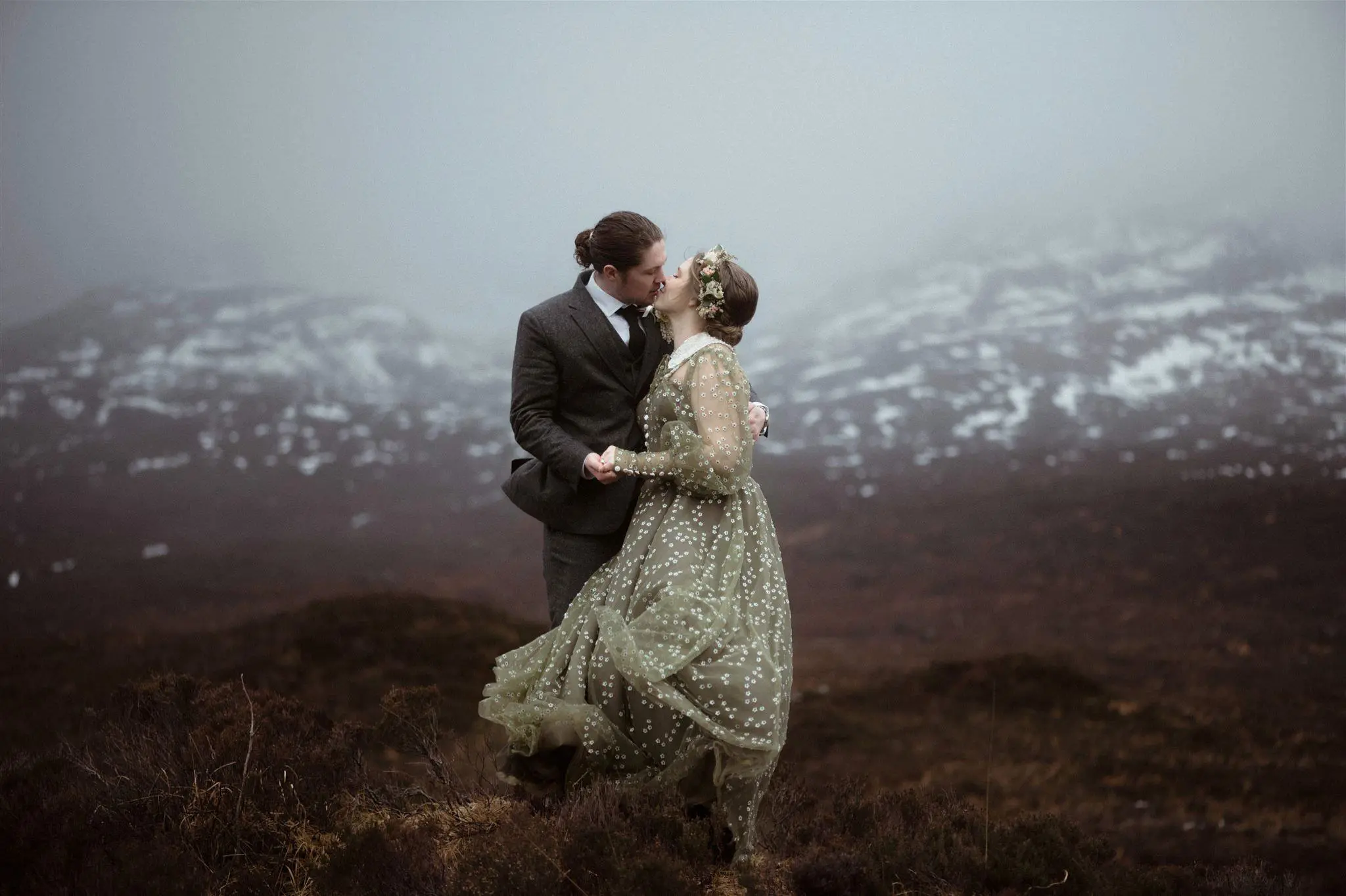 A couple embrace and kiss in a wintery Isle of Skye surrounded by snowy-covered mountains