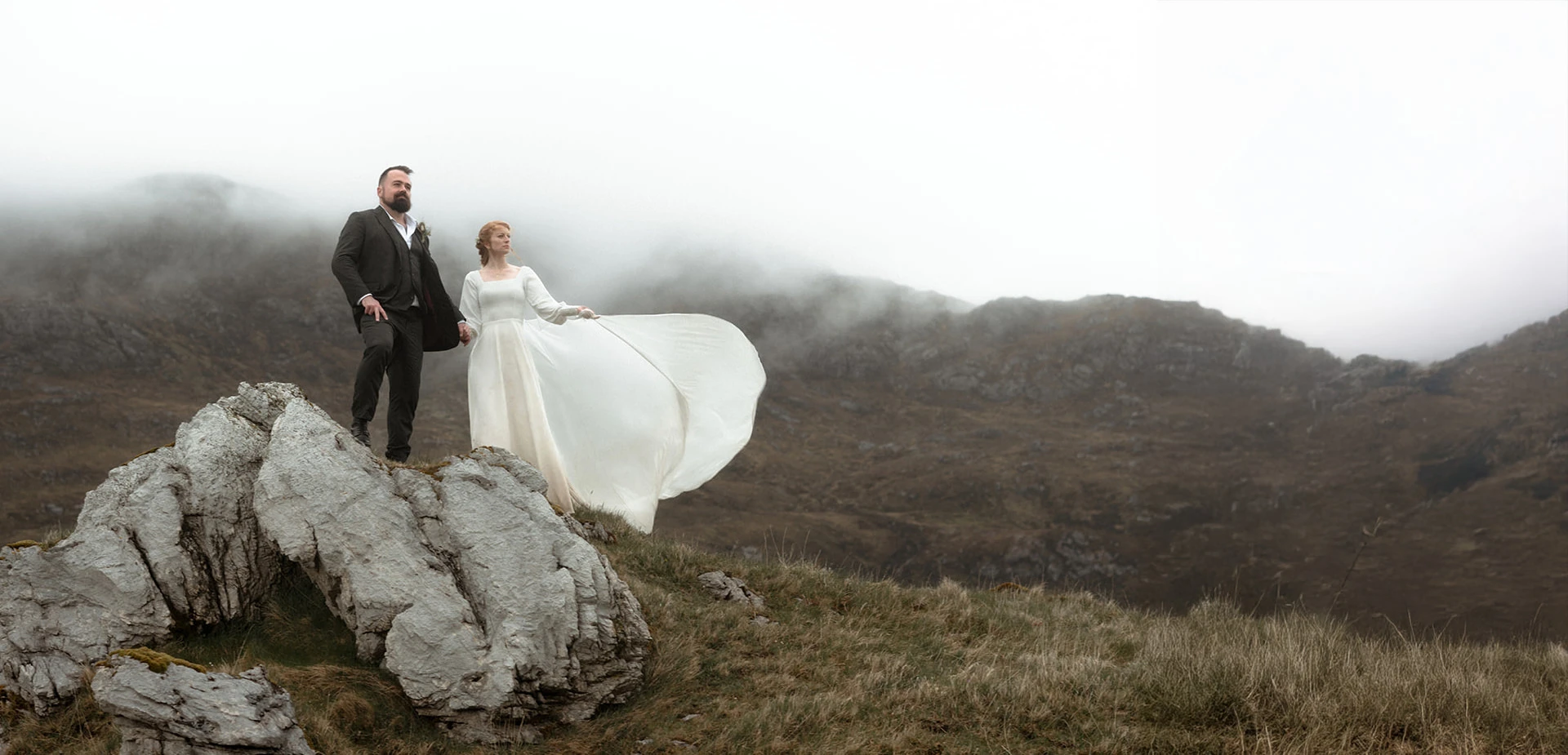 A young couple eloping in Scotland from the USA stand in front of a misty mountain